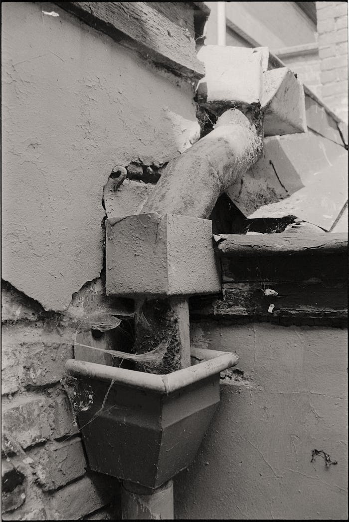 Close-up of a rusty drain pipe on a deteriorating building wall with visible damage.